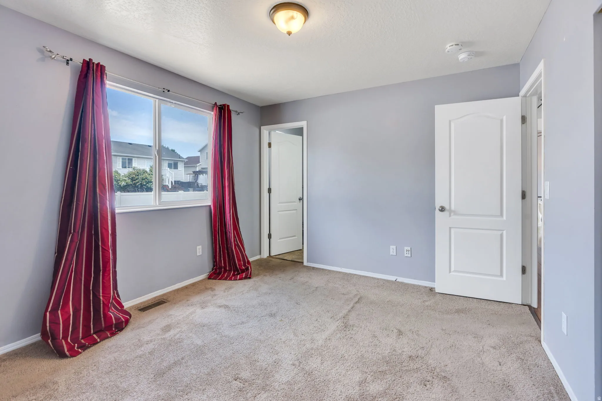 Spacious room with light gray walls, neutral carpeting, and a large window providing ample natural light