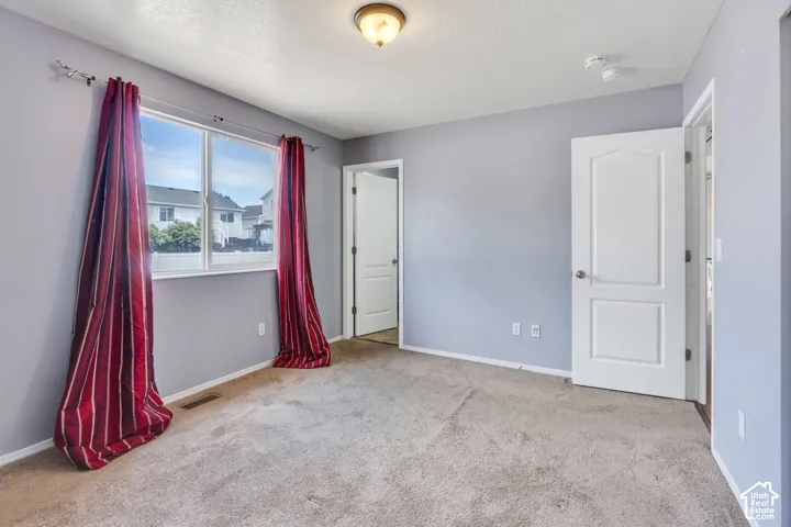 Spacious room with light gray walls, neutral carpeting, and a large window providing ample natural light