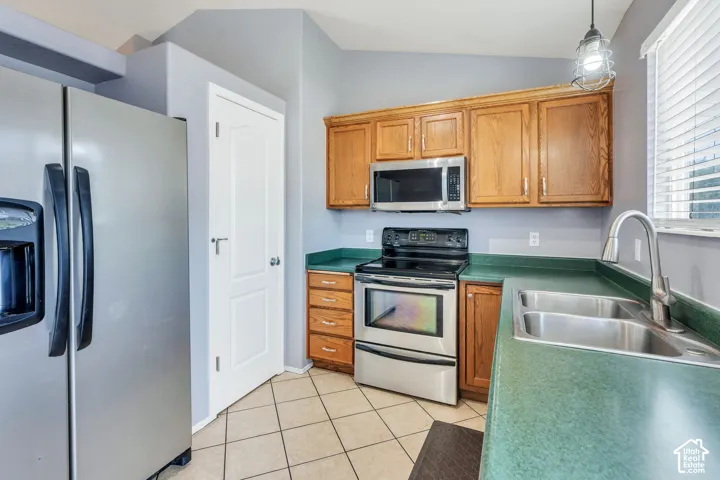 Kitchen featuring stainless steel appliances, wood cabinetry, a dual basin sink, and tile flooring