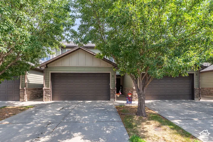 Green siding exterior with a dark brown garage door, stone accents, a concrete driveway, and mature trees