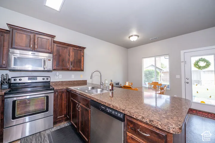 Kitchen featuring dark wood cabinetry, stainless steel appliances, a composite countertop, and an integrated kitchen island with a sink and dishwasher
