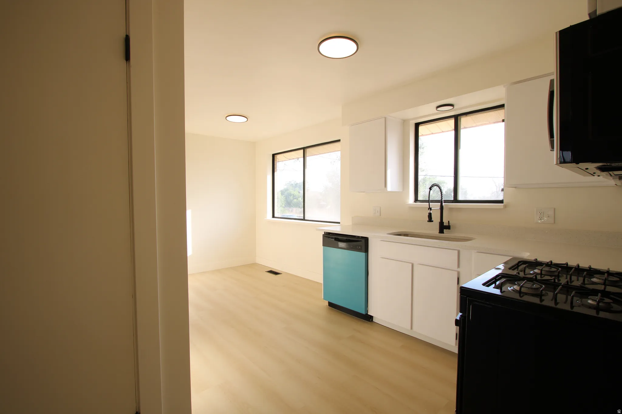 Open-concept kitchen and dining area featuring white cabinetry, light countertops, a black gas range, and a turquoise dishwasher