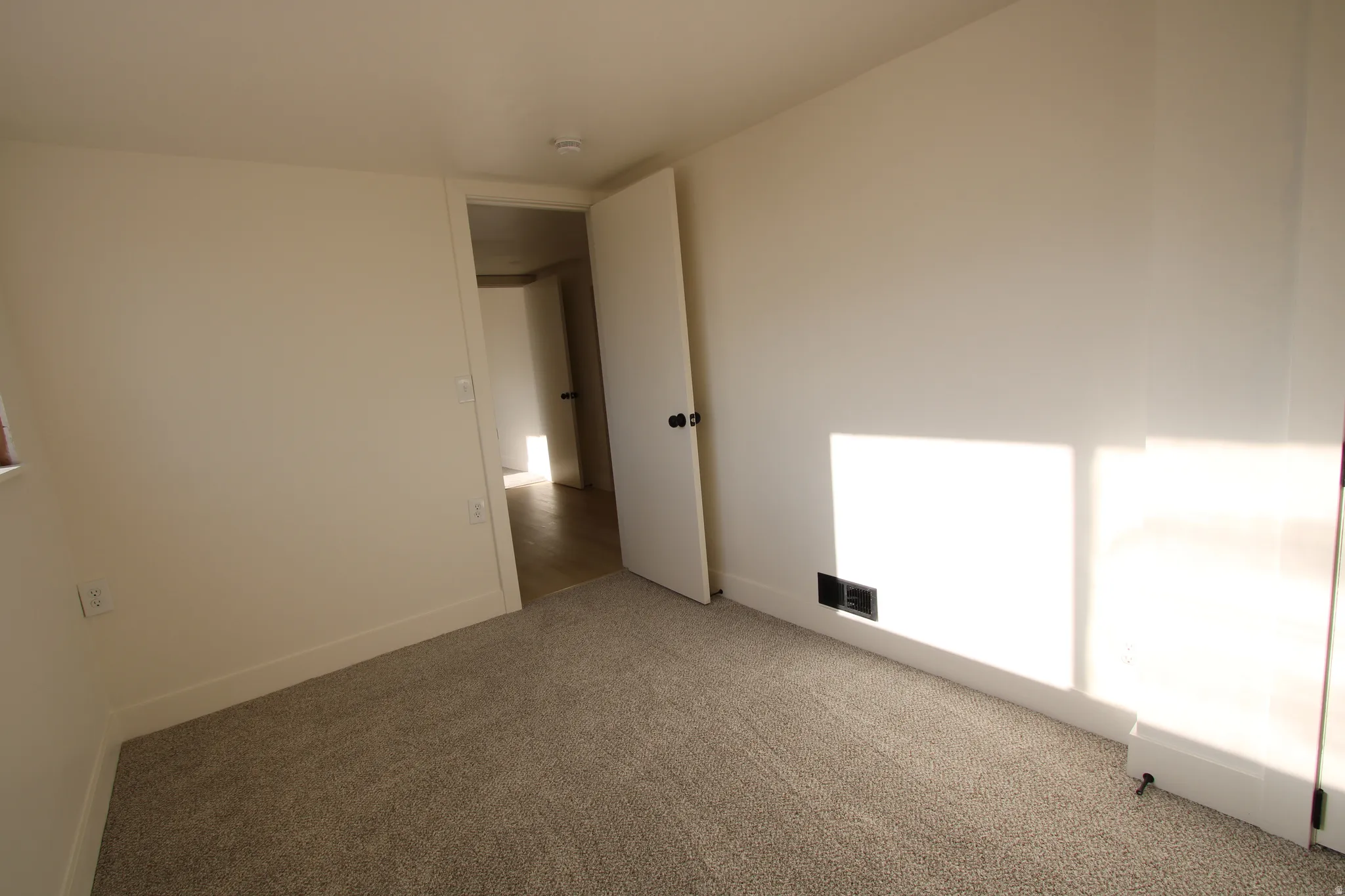 Carpeted room featuring light-toned walls, white baseboards, and a white interior door with a dark knob