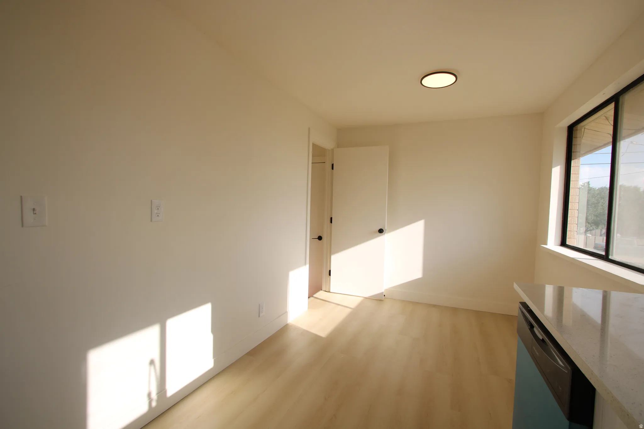 Bright room featuring light wood-finish flooring, a contemporary flush-mount ceiling light, white walls, and a large window with black framing