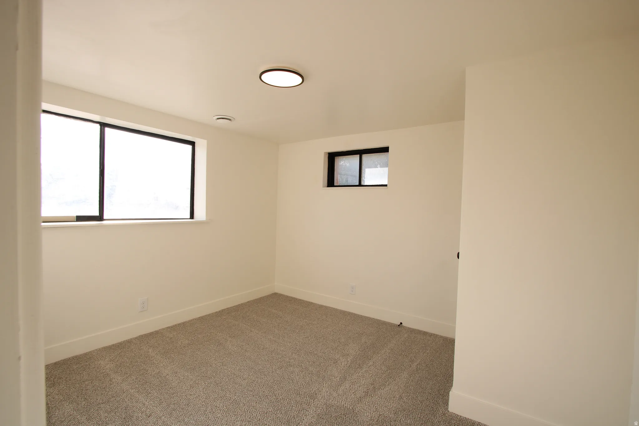 Clean interior space featuring light-colored walls and grey carpet flooring