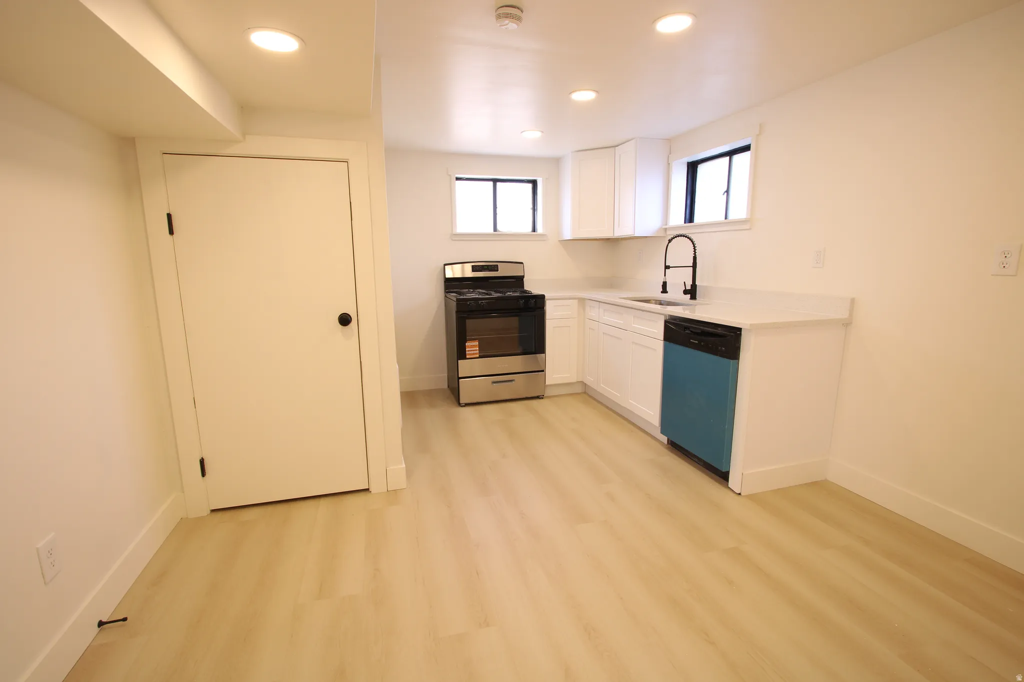 Kitchenette featuring white cabinetry, light-toned wood-finish flooring, and a stainless steel oven