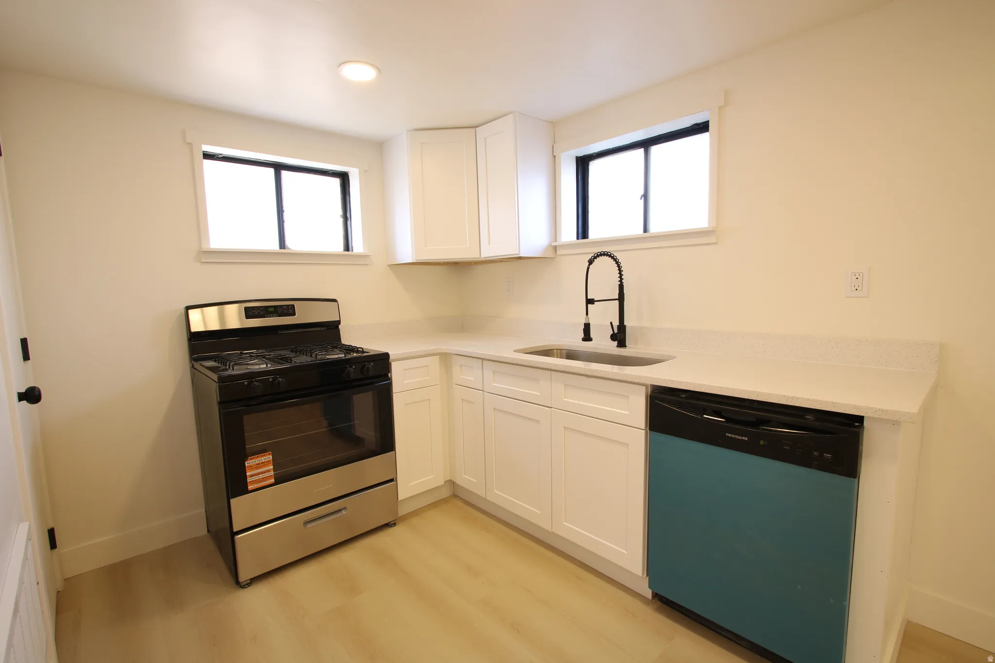 Contemporary kitchen featuring white cabinetry, light-toned countertops, a stainless steel gas range, a black dishwasher, and wood-finish flooring