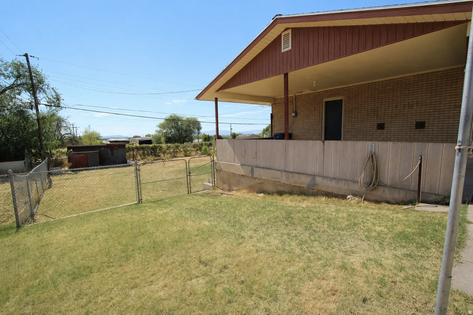 Expansive fenced yard featuring a covered porch with brick siding, a concrete patio, and mature landscaping