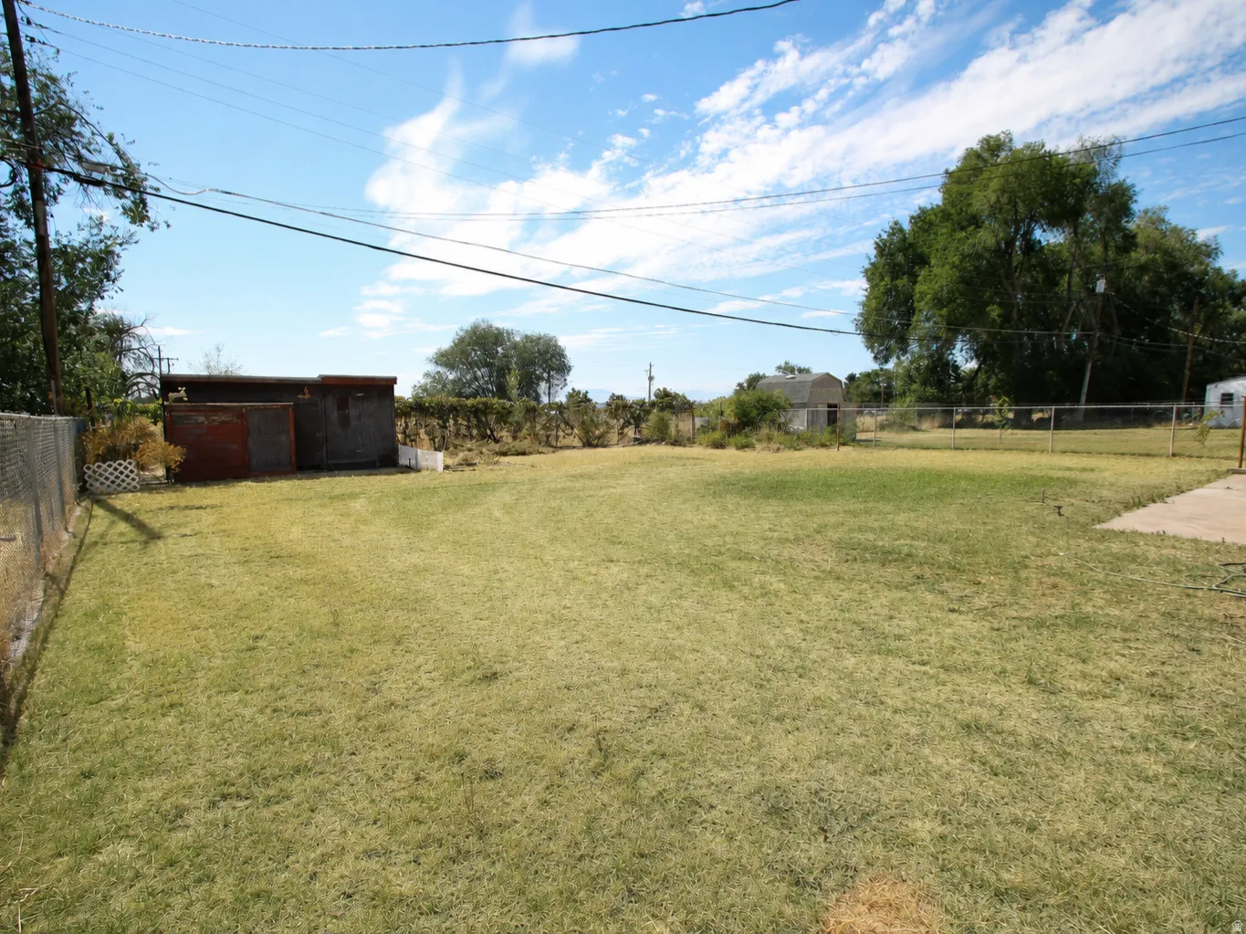 Expansive grassy lot with chain-link fencing, mature trees, and a concrete patio pad