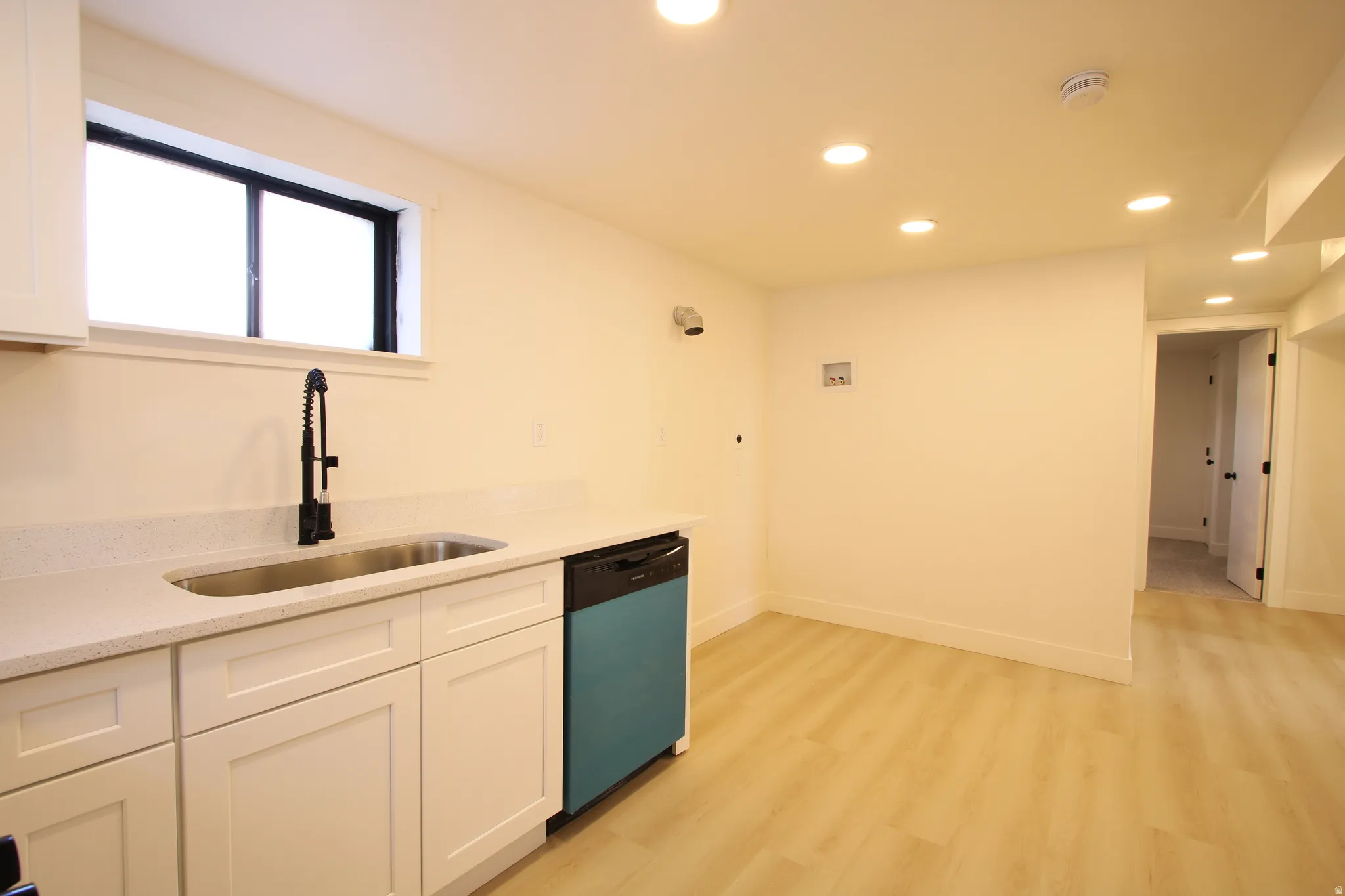 Kitchenette featuring light cabinetry, a stainless steel sink with a matte black pull-down faucet, and light-toned countertops
