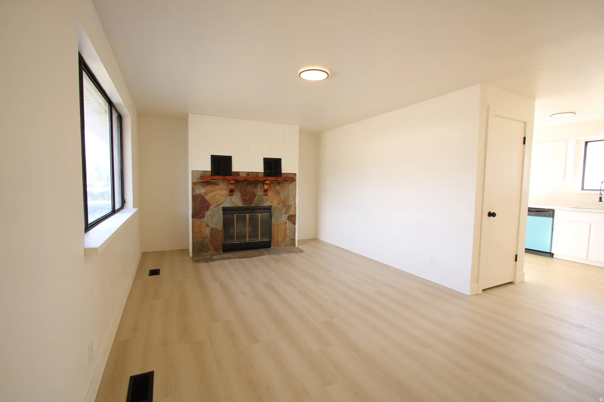 Living area featuring a stone fireplace with a wood mantle, wood-finish flooring, and white walls