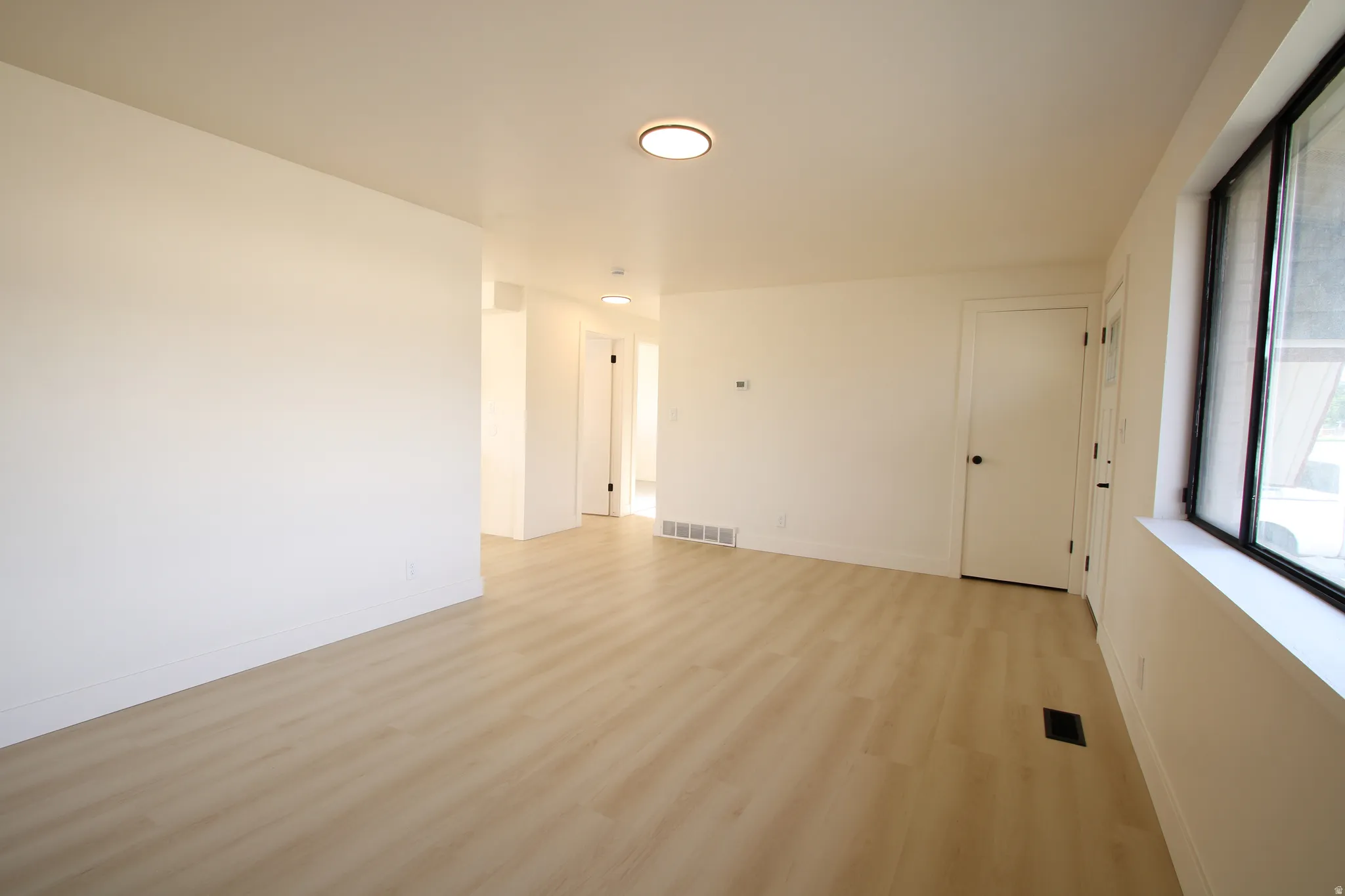 Bright interior space featuring light wood-finish flooring, white walls, and a large window with black framing
