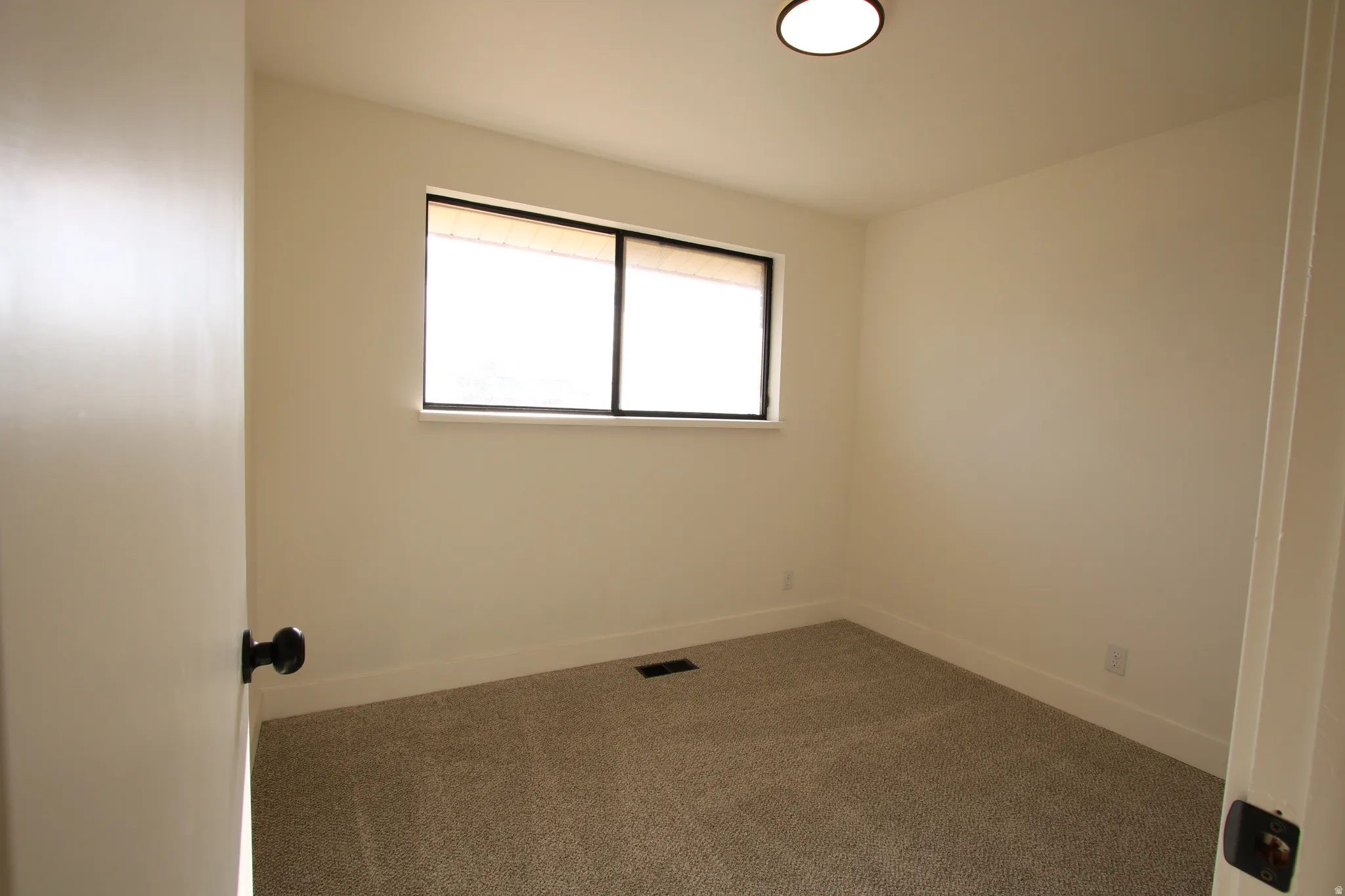 Room featuring neutral-toned walls, recessed window with a black frame, light-colored carpet, and a flush-mount ceiling light