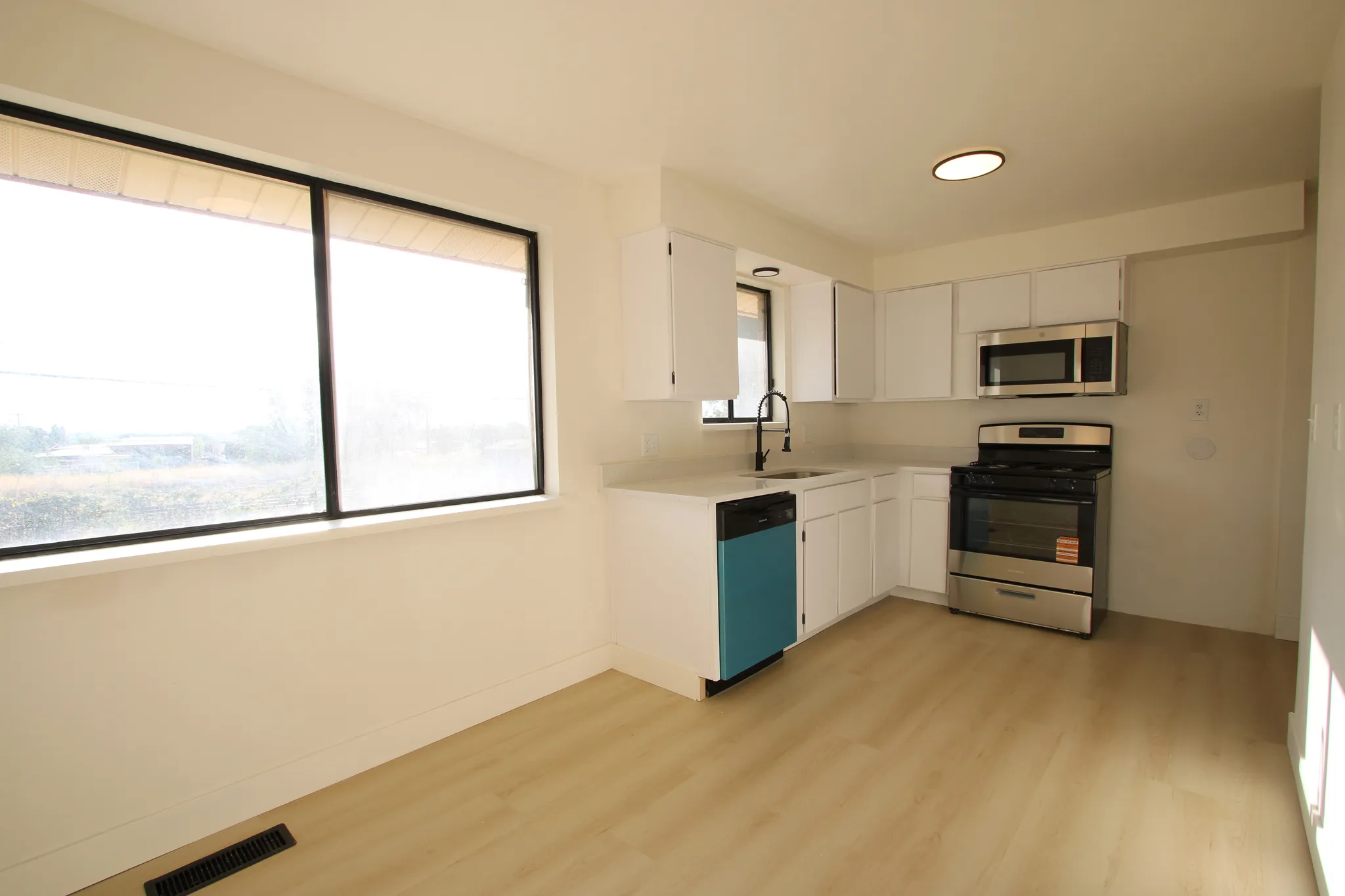 Kitchen featuring white cabinetry, light-toned countertops, wood-finish flooring, stainless steel appliances, and a large window