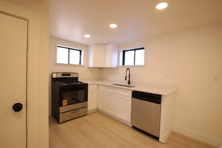 Updated kitchen featuring wood-finish flooring, recessed lighting, white cabinetry, stainless steel appliances, and a gooseneck faucet
