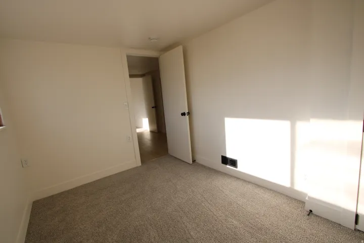 Carpeted room featuring light-toned walls, white baseboards, and a white interior door with a dark knob