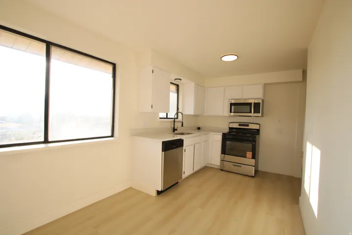 Kitchen featuring white cabinetry, stainless steel appliances, light-toned wood-finish flooring, and a large window