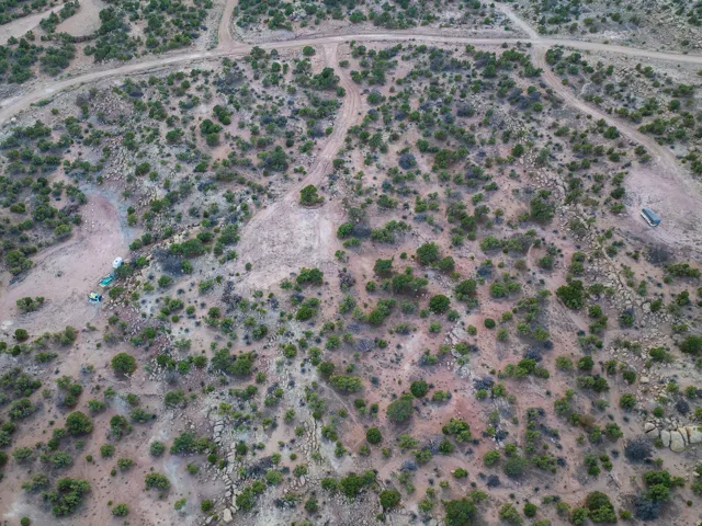 Expansive undeveloped land featuring natural terrain with scattered green foliage and visible unpaved paths
