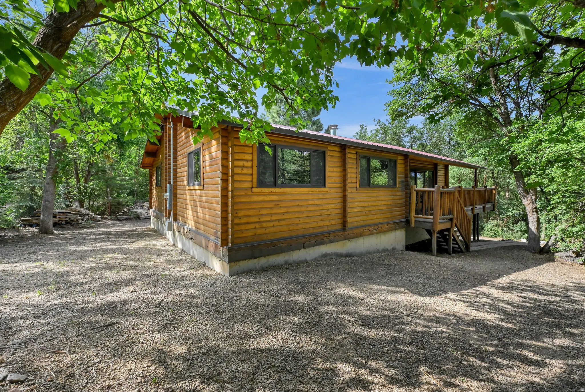 Log cabin exterior featuring a covered deck, wood siding, dark-framed windows, and a gravel lot