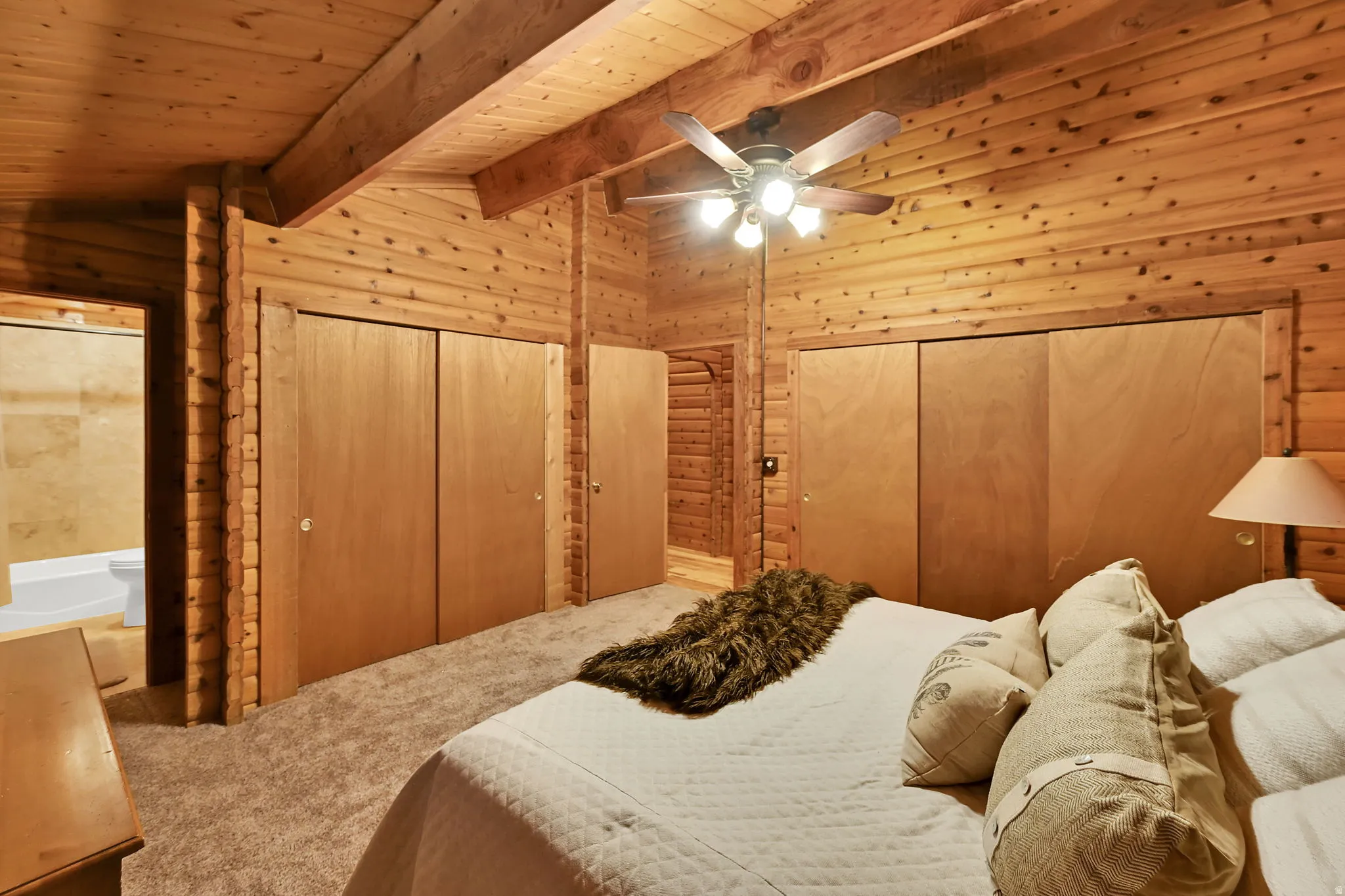 Wood-paneled room featuring a sloped wood-plank ceiling with exposed beams, ceiling fan light fixture, and two sets of bi-fold closet doors