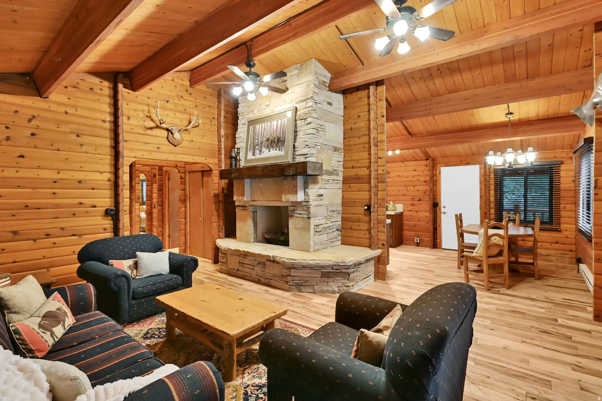 Spacious interior featuring natural wood-finish walls and ceilings with exposed beams, a central stone-clad fireplace with a hearth, and wood-finish flooring