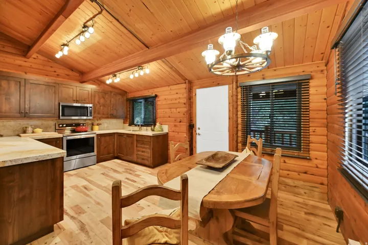 Open-concept kitchen and dining area featuring natural wood-finish walls and vaulted ceilings with exposed beams