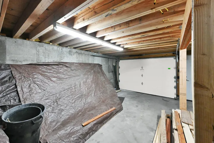 Exposed timber joist ceiling with fluorescent lighting illuminating concrete walls and a concrete floor