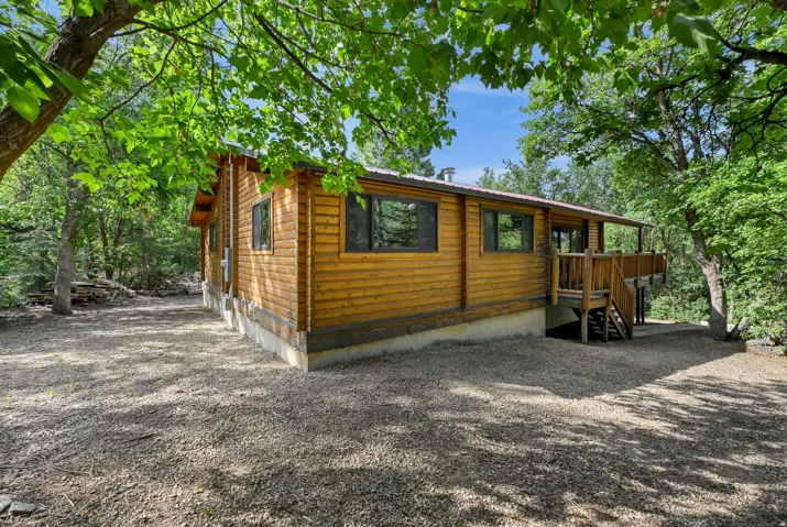 Log cabin exterior featuring a covered deck, wood siding, dark-framed windows, and a gravel lot
