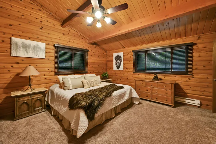 Wood-paneled room featuring a vaulted ceiling with exposed beams, ceiling fan, and two windows with dark wood blinds