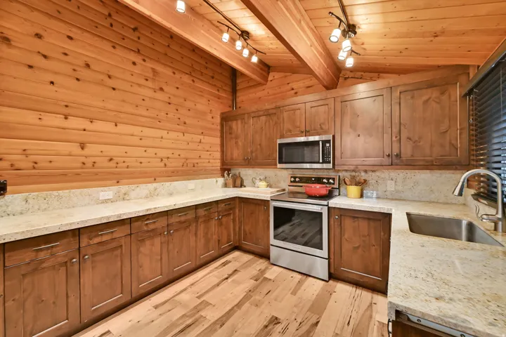 Open-concept kitchen featuring wood-finish flooring, light-toned countertops, wood cabinetry, and stainless steel appliances