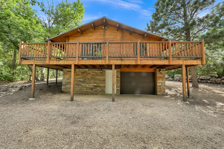 Rustic cabin-style residence featuring a prominent wood-finish balcony, a stone veneer foundation, and a dark garage door