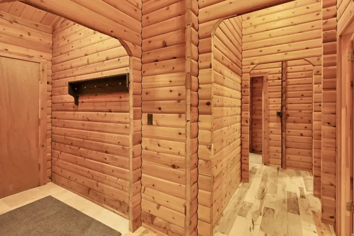 Wood-paneled hallway featuring arched doorways, wood-finish flooring, a built-in coat rack, and natural wood doors