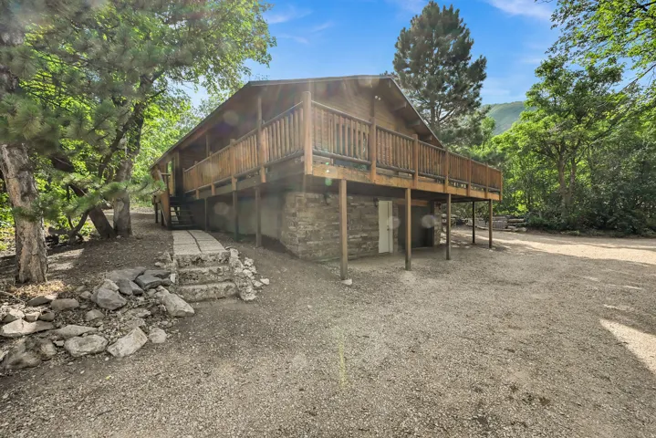 Wood-sided property featuring a raised deck with wooden railing and support posts, a stone foundation, and a gravel driveway