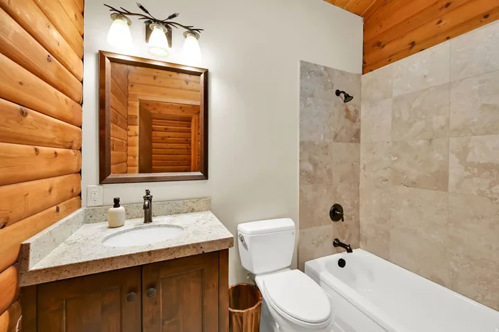 Bathroom featuring a wood-panel wall, corner vanity with granite countertop, integrated sink, bronze-finish faucet, and a framed mirror