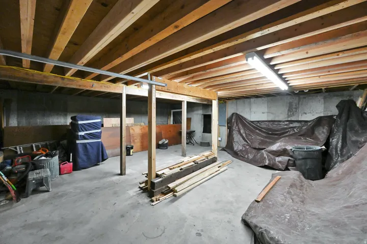Unfinished basement featuring exposed wood ceiling joists, concrete flooring, concrete block walls, and fluorescent lighting fixtures