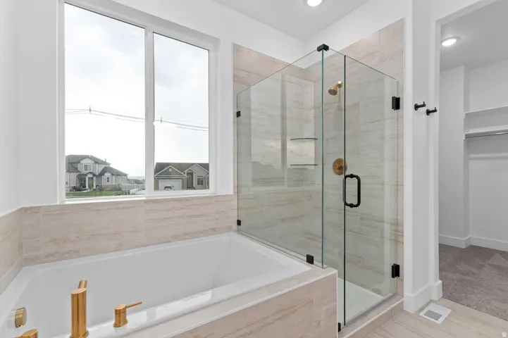 Soaking tub with brass-finish fixtures, surrounded by light-toned tile, alongside a glass-enclosed shower featuring a brass-finish rain shower head and matte black hardware