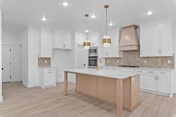 Contemporary kitchen featuring a light wood-finish island with a white countertop, brass pendant lighting, built-in double ovens, and a tile backsplash
