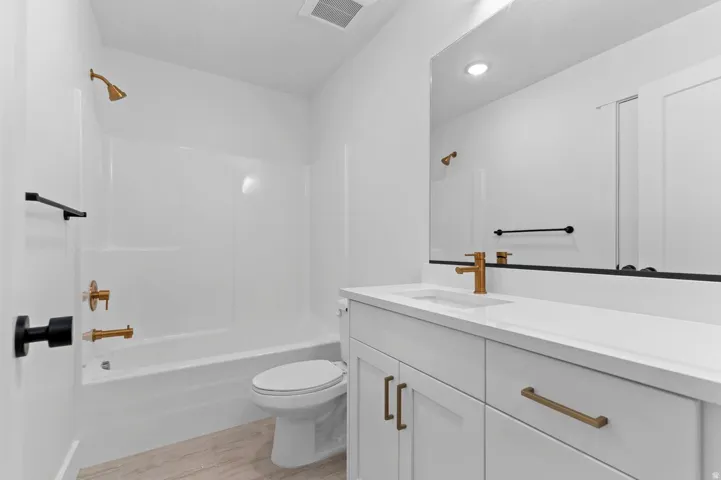 Bathroom featuring a white vanity with integrated sink, gold-toned faucet, and a large wall-mounted mirror