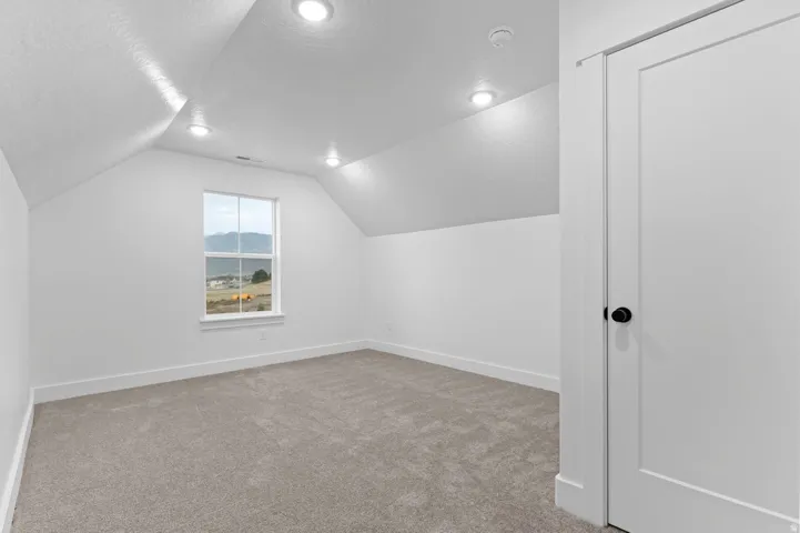 Spacious room featuring vaulted ceilings, recessed lighting, neutral carpeting, and a window with mountain scenery