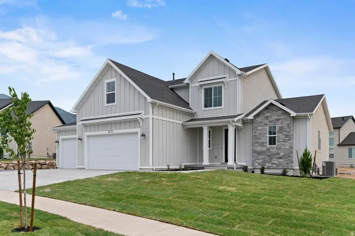 Modern farmhouse exterior featuring board and batten siding, stone accents, a covered entry, a two-car garage, and a manicured lawn