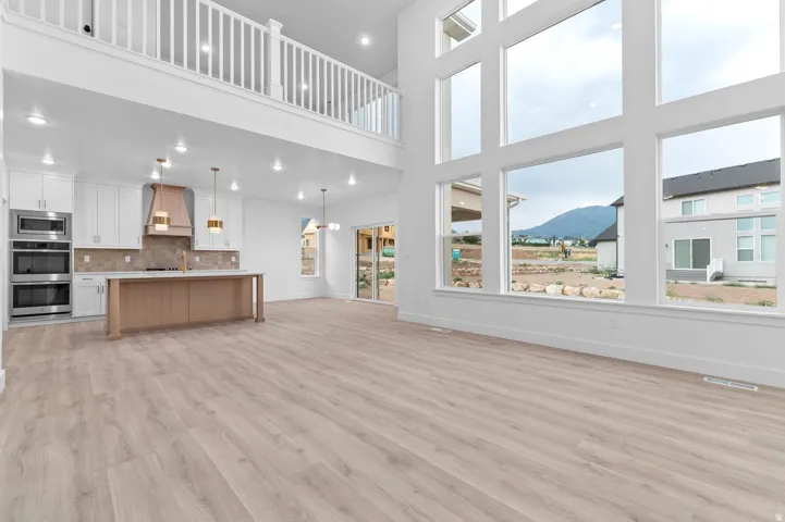 Spacious living area featuring expansive two-story windows, light wood-finish flooring, and a contemporary kitchen with white cabinetry and an island