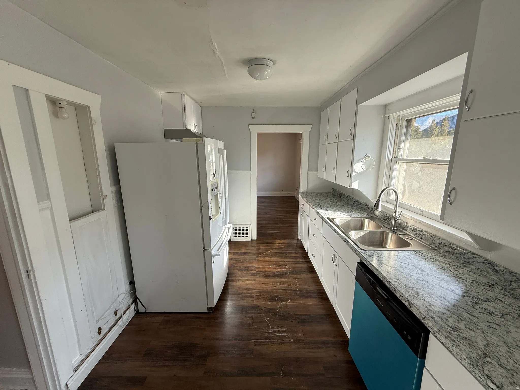 Galley kitchen featuring wood-finish flooring, white cabinetry, a double basin stainless steel sink, and light-toned countertops