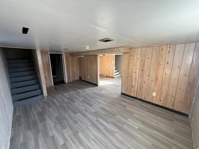 Open finished basement space featuring wood-finish paneling, light-toned plank flooring, and painted stairs
