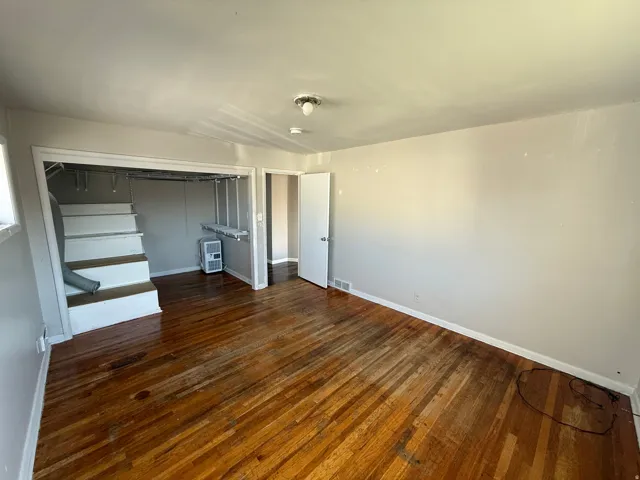 Wood-finish flooring throughout, featuring a staircase with white risers and a white door leading to another area