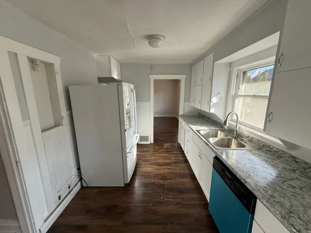 Galley kitchen featuring wood-finish flooring, white cabinetry, a double basin stainless steel sink, and light-toned countertops