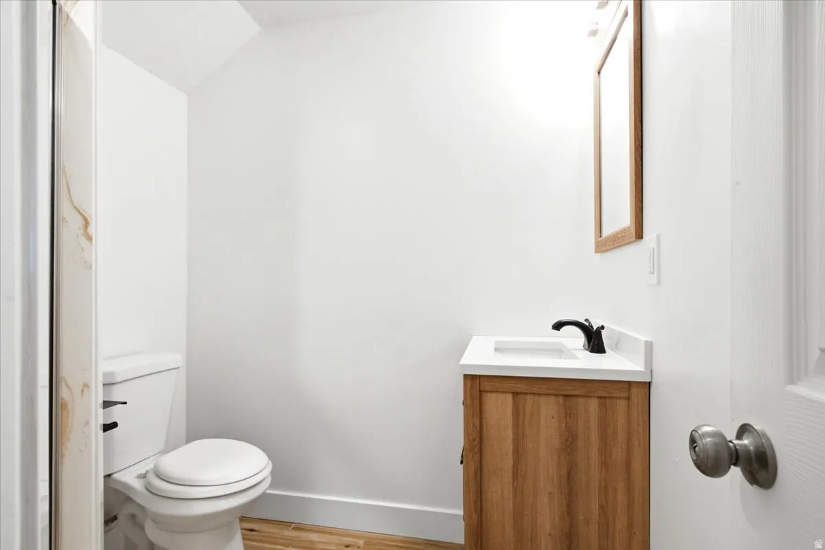 Wood-finish flooring, white walls, and a wood-frame mirror over a vanity with a white countertop and black faucet