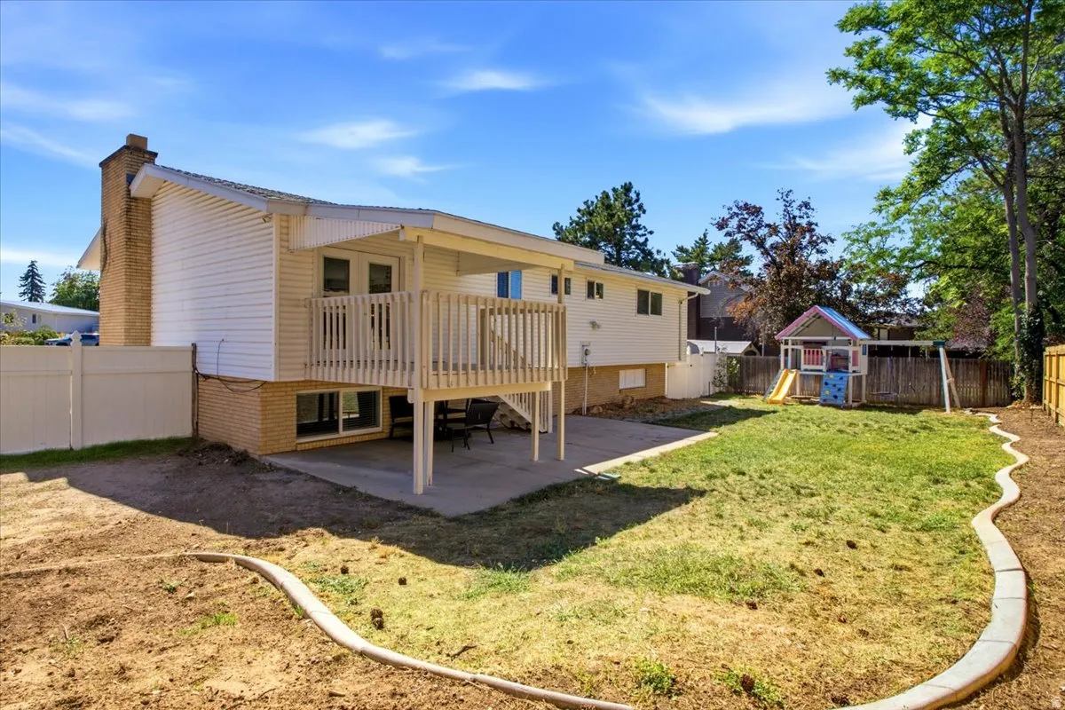 Exterior featuring white siding, a brick chimney, a wood deck with railings, and a concrete patio