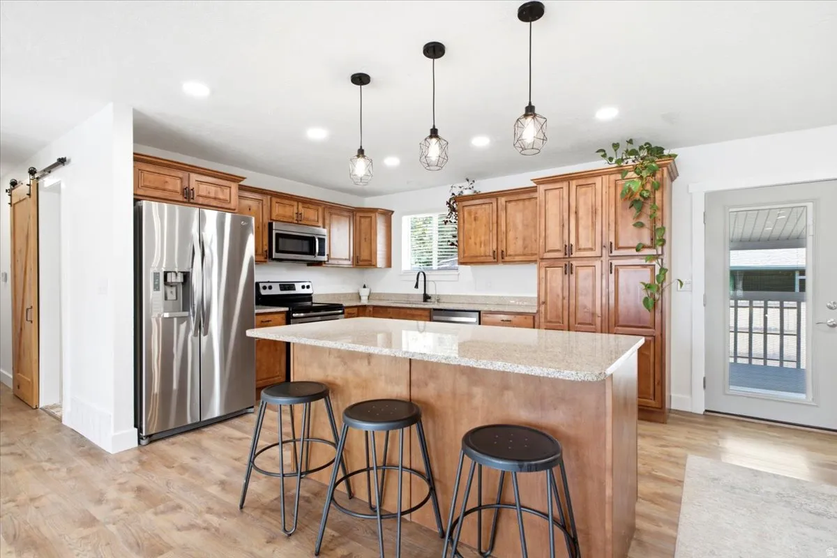 Kitchen with stainless steel appliances, wood-finish cabinetry, a central island with a light-toned countertop, and wood-finish flooring
