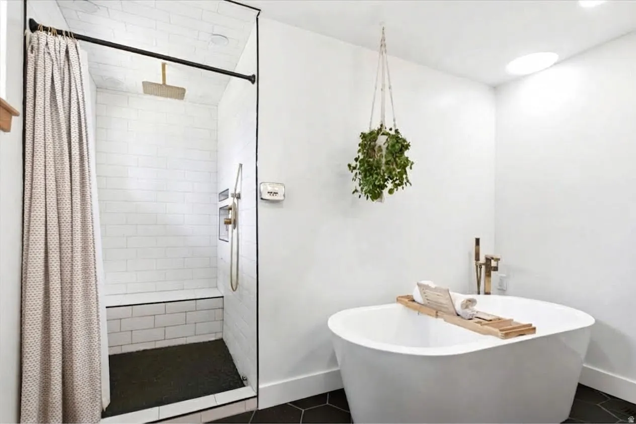 Freestanding soaking tub with floor-mounted brass fixtures, separate shower with subway tile surround and integrated bench, and black hexagonal floor tiling
