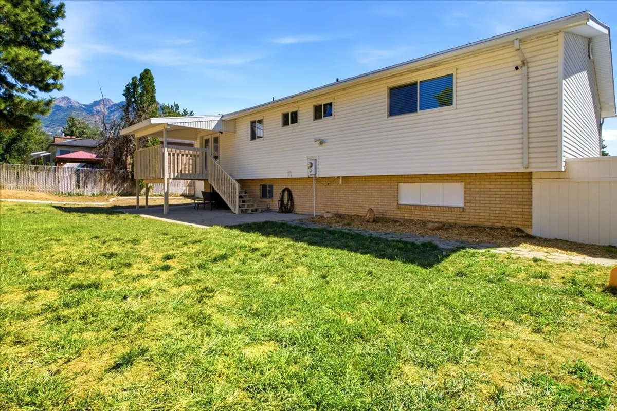 Expansive grassy yard with a raised deck, concrete patio, and mature trees